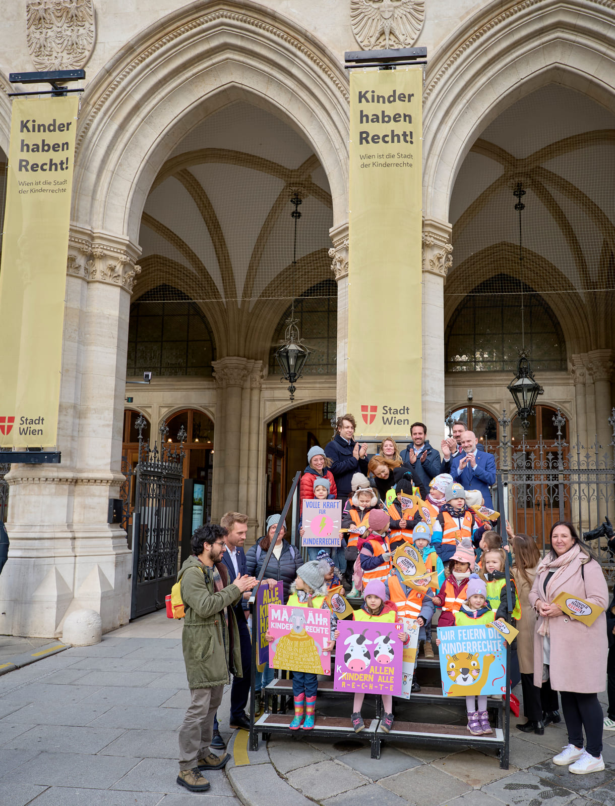 Gruppenfoto vor einem der Seiteneingänge des Wiener Rathauses mit Kinderrechte-Fahnen