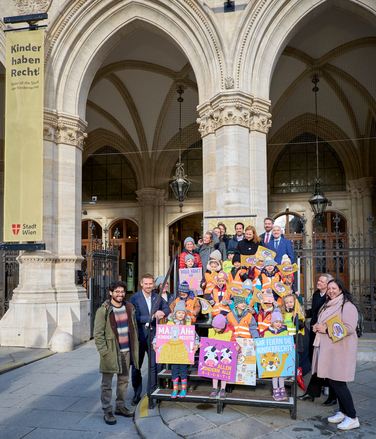 Gruppenfoto vor einem der Seiteneingänge des Wiener Rathauses mit Kinderrechte-Fahnen