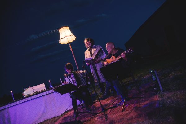 Nora Winkler am Akkordeon, Martin Brachvogel mit dicker Mappe und Robert Lepenik an der Gitarre vor der kleinen Bühne mit Kartonhaus-Modell