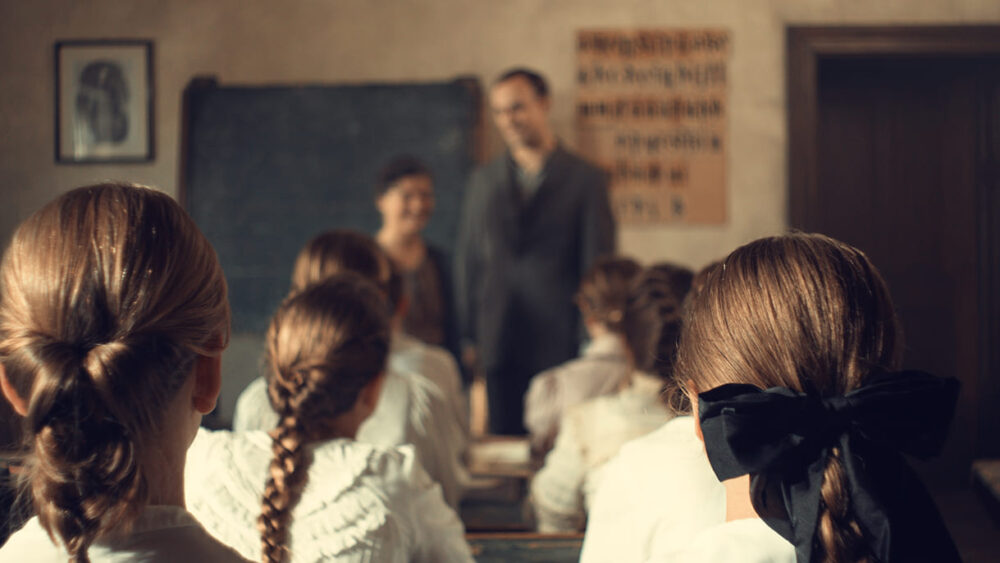 Bild aus dem Film: Darstellerin der Eugenie Schwarzwald mit Oskar-Kokoschka-Darsteller vor den Darstellerinnen der Schulklasse