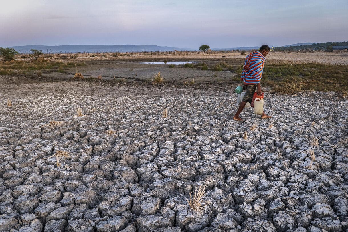 Ein Mann, der Kanister mit Wasser trägt, läuft während der Trockenzeit am 23. September 2022 über trockenes Ackerland in Bena, Regierungsbezirk Tengah in Südtimor, Provinz Ost-Nusa Tenggara, Indonesien.