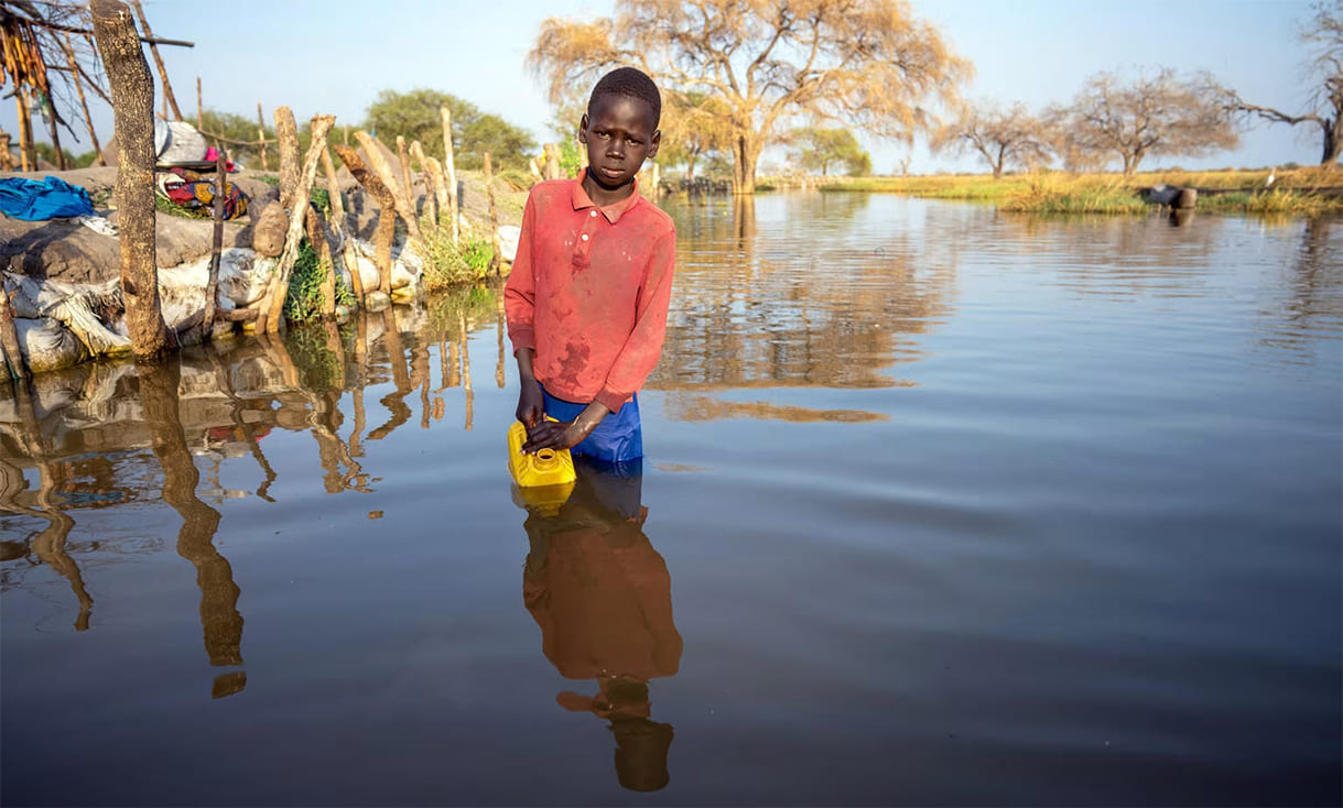 Unicef-Foto aus dem Südsudan klarerweise nciht von der bevorstehenden Katastrophe, Kind steht voll angezogen im Wasser und versucht mit einem Kanister Wasser zu schöpfen