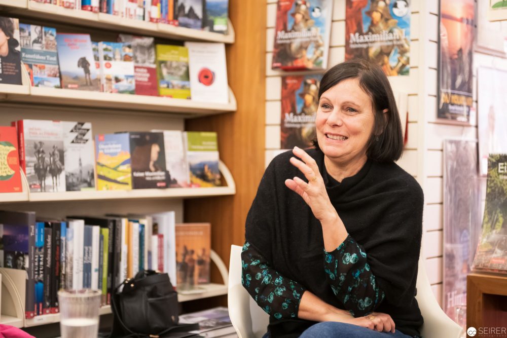 Die Illustratorin und Autorin Linda Wolfsgruber sitzt neben einem Regal mit vielen Büchern