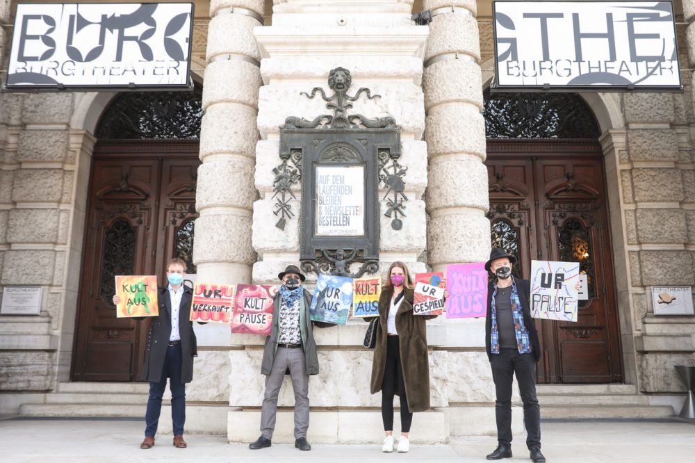 Vier Menschen vor dem geschlossenen Burgtheater. Sie halten Tafeln auf denen sie die Öffnung von Kunst und Kultur als erste nach dem Lockdown fordern