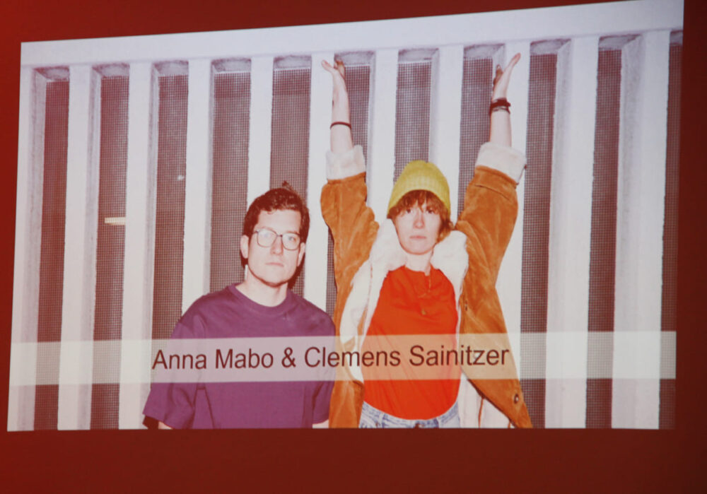 Vorher angefertigtes Foto des Künstler:innenduos Anna Mabo und Clemens Sainitzer - eingeblendet auf den Screens an den Wänden