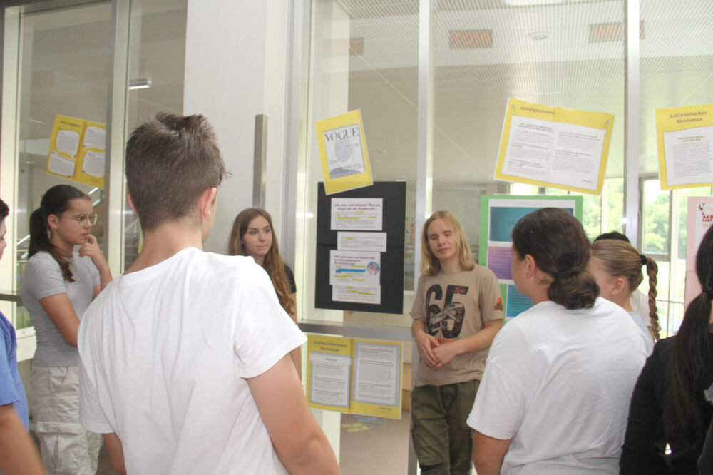 Jugendliche begleiten jüngere Schüler:innen durch die selbst gestaltete Antirassismus-Ausstellung