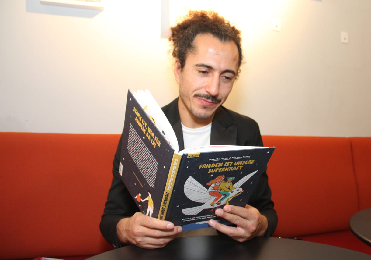 Autor Omar Khir Alanam mit dem offenen Buch "Frieden ist unsere Superkraft"