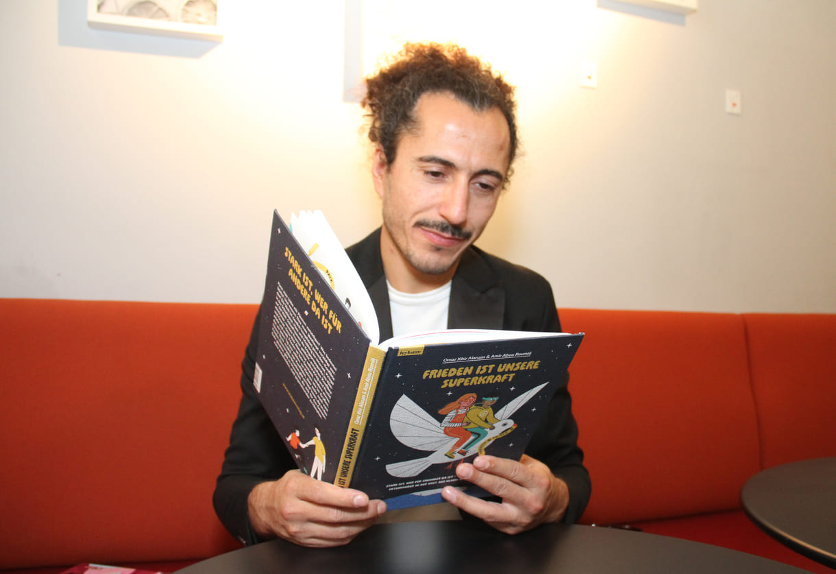 Autor Omar Khir Alanam mit dem offenen Buch "Frieden ist unsere Superkraft"