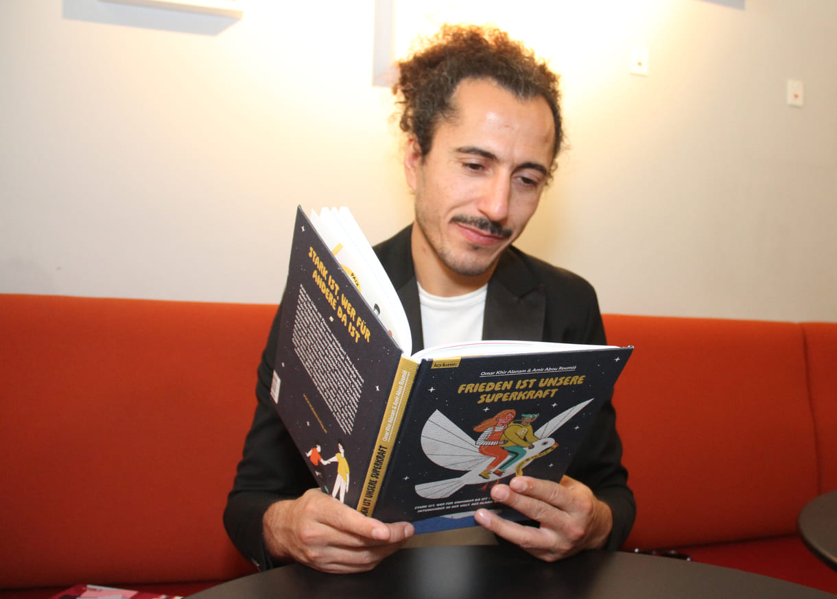 Autor Omar Khir Alanam mit dem offenen Buch "Frieden ist unsere Superkraft"