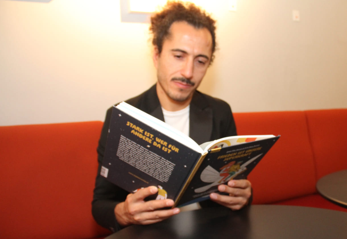 Autor Omar Khir Alanam mit dem offenen Buch "Frieden ist unsere Superkraft"