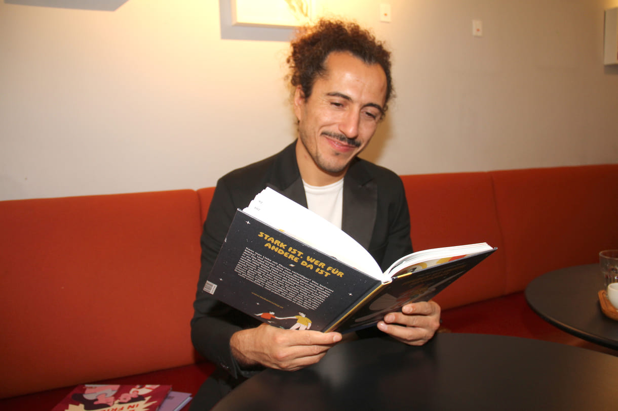 Autor Omar Khir Alanam mit dem offenen Buch "Frieden ist unsere Superkraft"