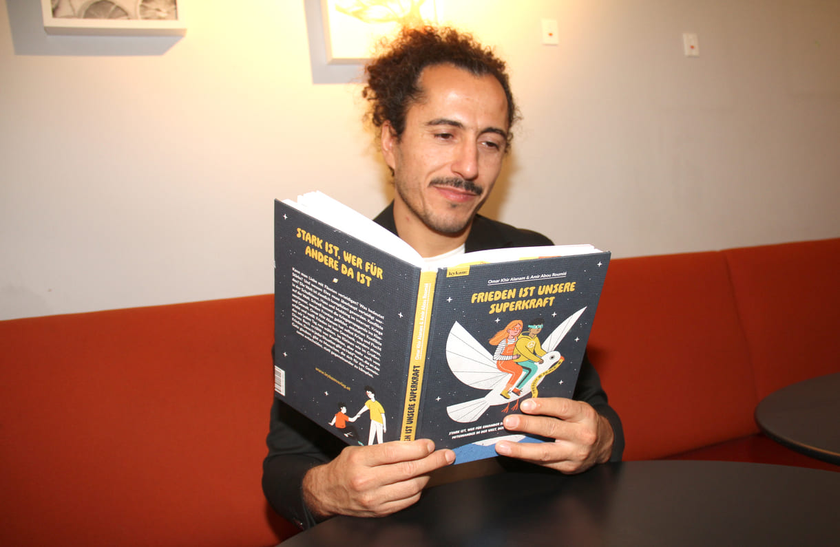 Autor Omar Khir Alanam mit dem offenen Buch "Frieden ist unsere Superkraft"