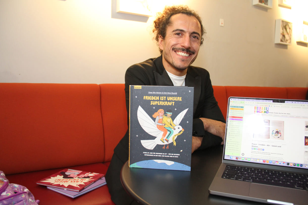 Autor Omar Khir Alanam mit seinem jüngsten Buch "Frieden ist unsere Superkraft" und dem geöffneten Laptop von KiJuKU, wo das Interview mitgeschrieben wurde