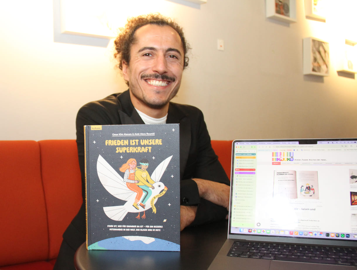 Autor Omar Khir Alanam mit seinem jüngsten Buch "Frieden ist unsere Superkraft" und dem geöffneten Laptop von KiJuKU, wo das Interview mitgeschrieben wurde
