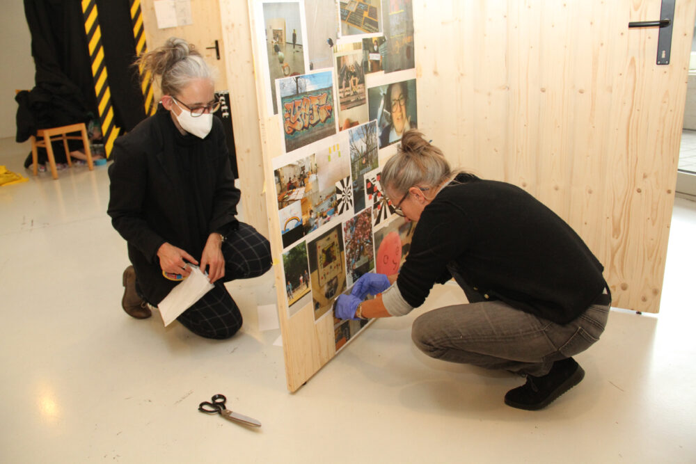 Von Jugendlichen ausgewählte Fotos werden an Holzwände geklebt