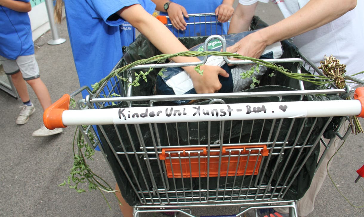 Kinder befüllen den Einkaufswagen mit Granulat und Erde und beschriften den Haltegriff