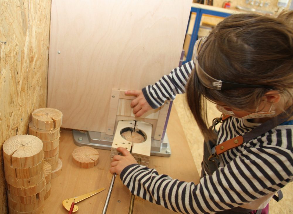 Mädchen bohrt mit Standbohrmaschine (schutz-ummantelt) Loch in runde Holz-Scheibe