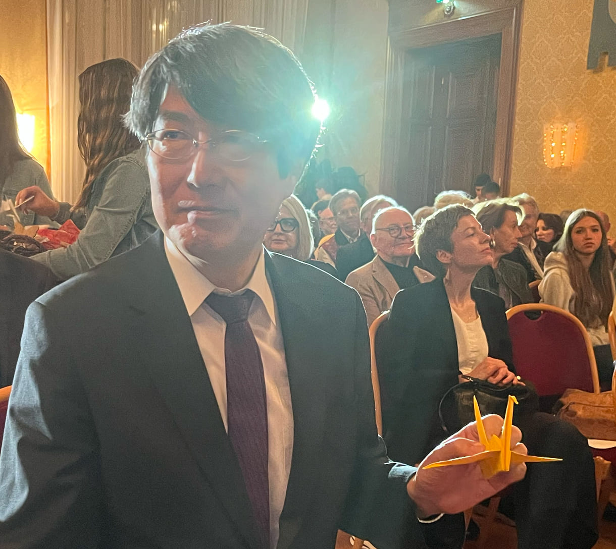 Japans Botschafter in Österreich, Iwama Kiminori , hält seinen von Schüler:innen bekommenen Papierkranich in Richtung Kameras