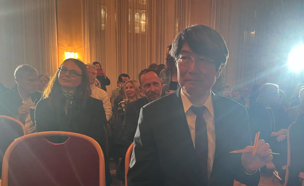 Japans Botschafter in Österreich, Iwama Kiminori , hält seinen von Schüler:innen bekommenen Papierkranich in Richtung Kameras