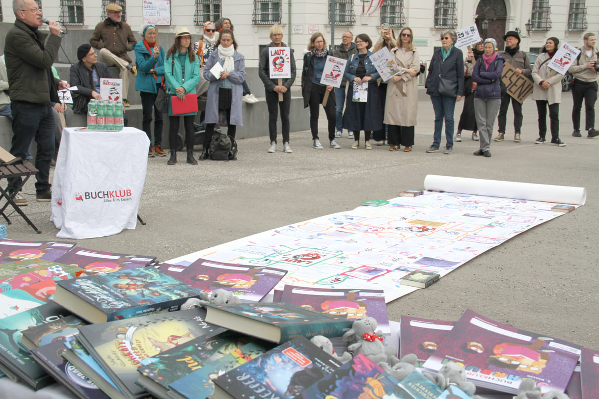 Bücher - zur freien Entnahme - die künstlerisch gestaltete laaaange Papierraolle und Demonstrant:innen mit Sprüchen auf Kartontafeln