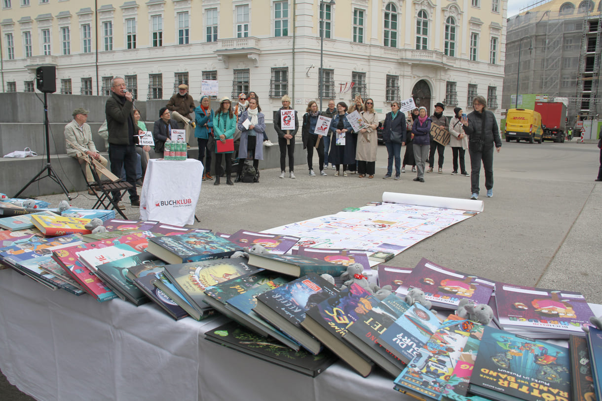 Bücher - zur freien Entnahme - die künstlerisch gestaltete laaaange Papierraolle und Demonstrant:innen mit Sprüchen auf Kartontafeln