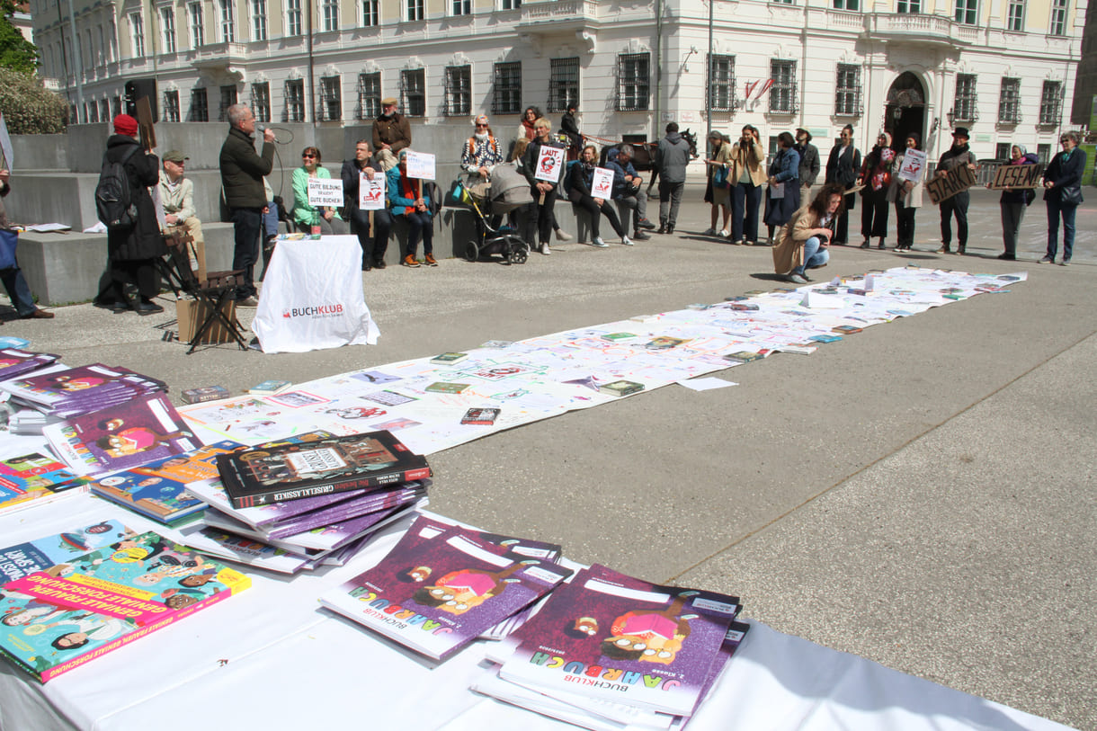 Bücher - zur freien Entnahme - die künstlerisch gestaltete laaaange Papierraolle und Demonstrant:innen mit Sprüchen auf Kartontafeln