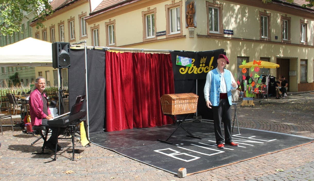 Kranner auf der Bühne, rechts im Hintergrund der Stand mit Friedens-Zeichen, -Puzzles, - Ketten...