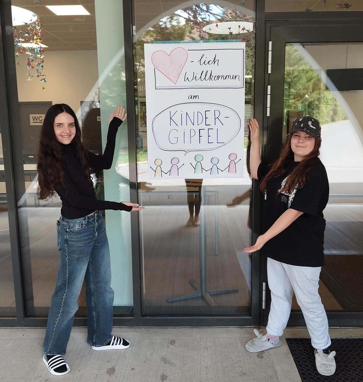 Isabel und Lina mit einem Herzlich-willkommen-Plakat zum Kindergipfel
