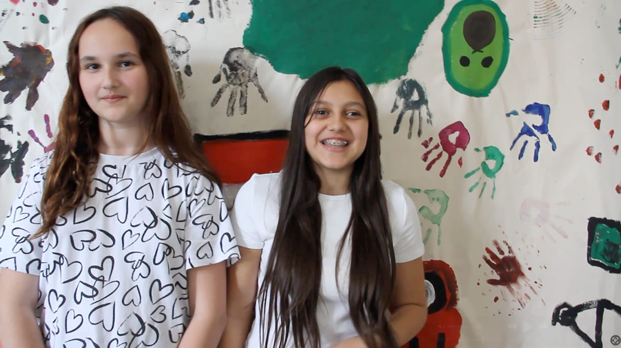 Lena und Amina im Video-Interview (Screenshot) vor dem Stoffbanner, das ihre Gruppe in einer der Fail-Stunden gemalt hatte - und das nach einigen Wochen gegen ein zweites der anderen Gruppe ausgetauscht wird