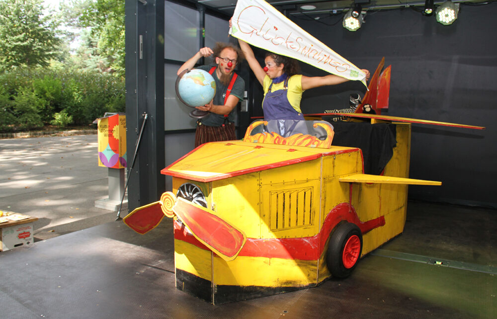 Eva Zarbl (rechts) und Andi Geyer (links) als Clownin Paula und Clown Fu mit ihrem hölzernen Flugzeug und einem Globus des Stücks 