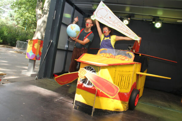 Eva Zarbl (rechts) und Andi Geyer (links) als Clownin Paula und Clown Fu mit ihrem hölzernen Flugzeug und einem Globus des Stücks "Gemeinsam zum Glück stolpern ..."