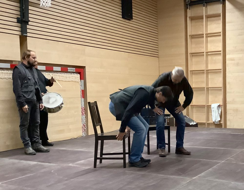 Szenenfoto: Künstler kommen mit Stühlen auf die Bühne