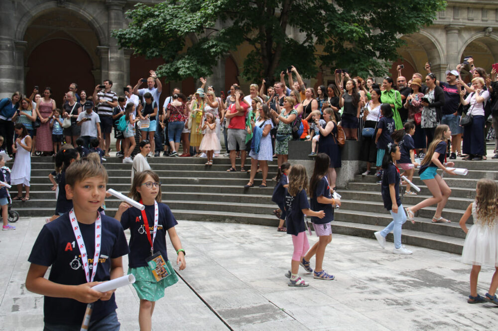 Eltern begrüßen ihre frischgebackenen Absolvent:innen der Kinderuni jubelnd im Arkadenhof der Universität Wien