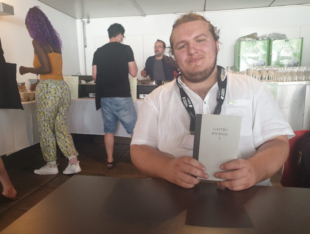 Jugendlicher mit einem Buch, in dem er selbst einen Beitrag veröffentlicht hat im Festival-Restaurant