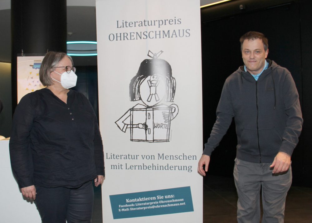 Hauptpreisträger Michael Wilhelm neben einem Plakat des Literaturpreises 