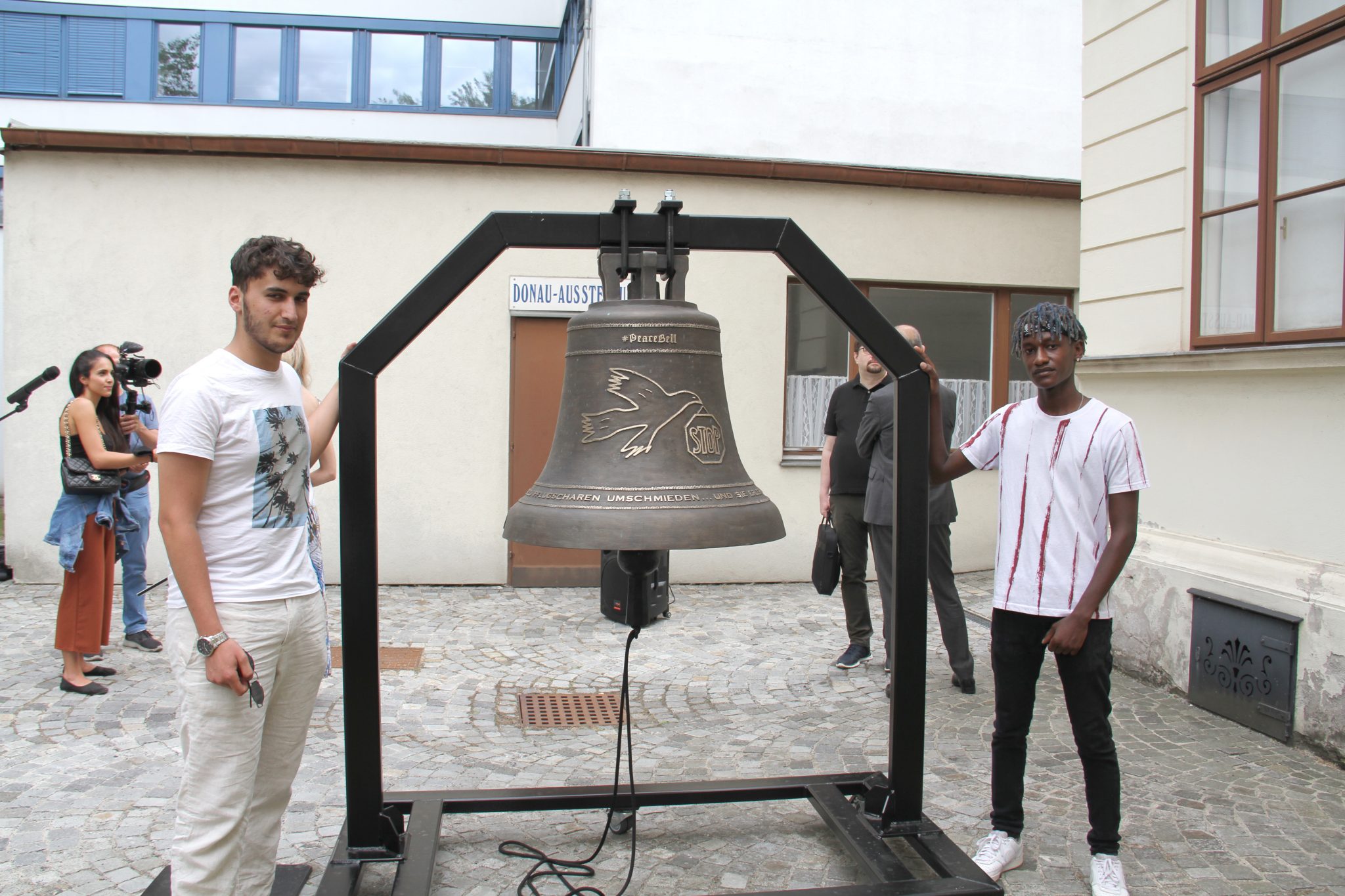 Ucar Abdulvedut und Gibra Mwasi mit der Friedensglocke und dem Gestell, in dem sie aufgehängt ist
