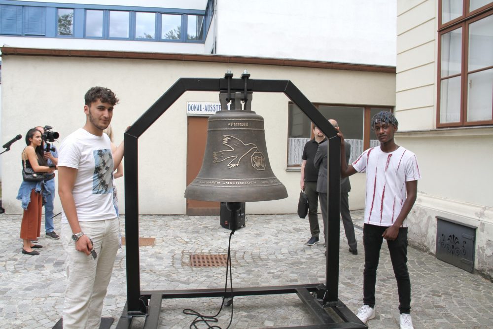 Ucar Abdulvedut und Gibra Mwasi mit der Friedensglocke und dem Gestell, in dem sie aufgehängt ist