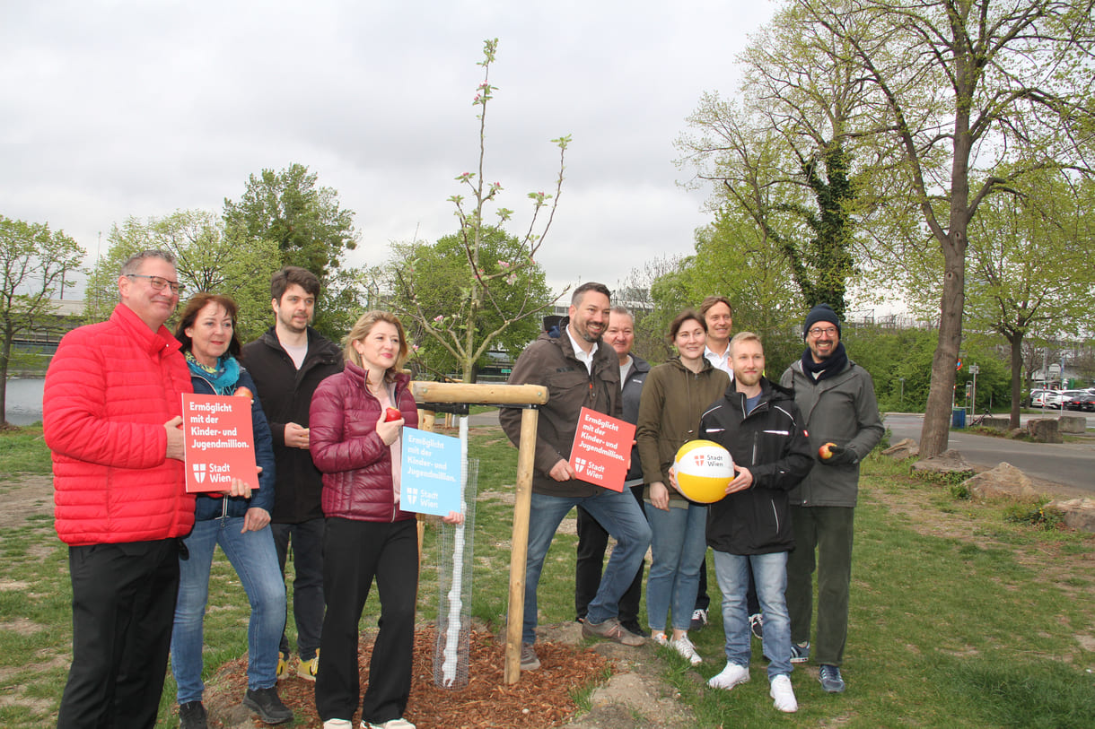 Dieser - und 39 weitere Apfelbäume hier bei der U6-Station Neue Donau wurden durch eines der Projekte aus der Kinder- und Jugendmillion verwirklicht - darauf weisen einige bei diesem Großgruppenfoto auf Tafeln hin