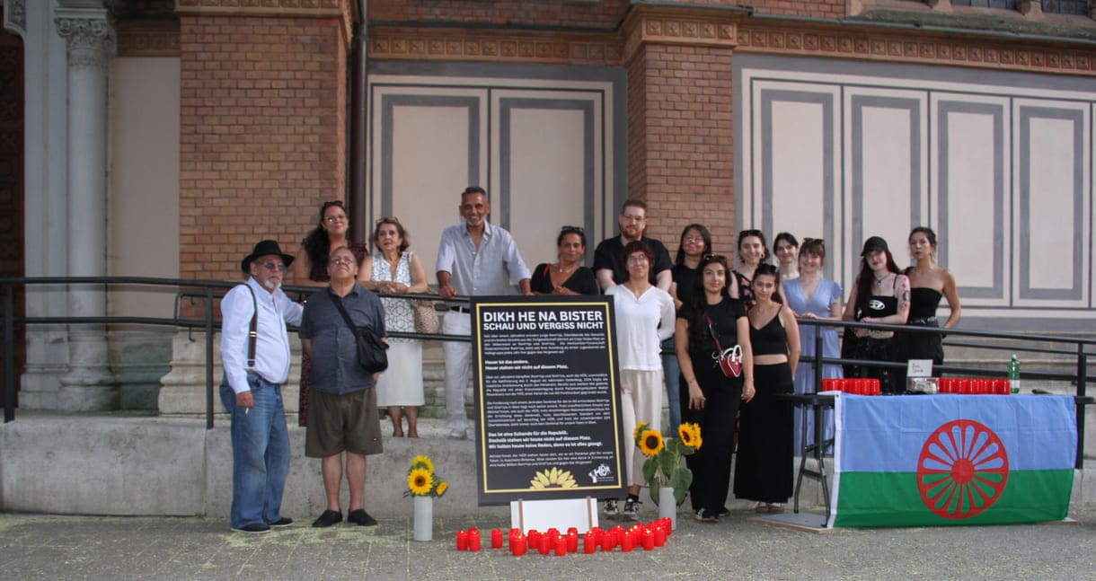 Aktivist:innen und Gedenk-Gäst:innen zwischen Kirche und Plakat sowie Infotisch