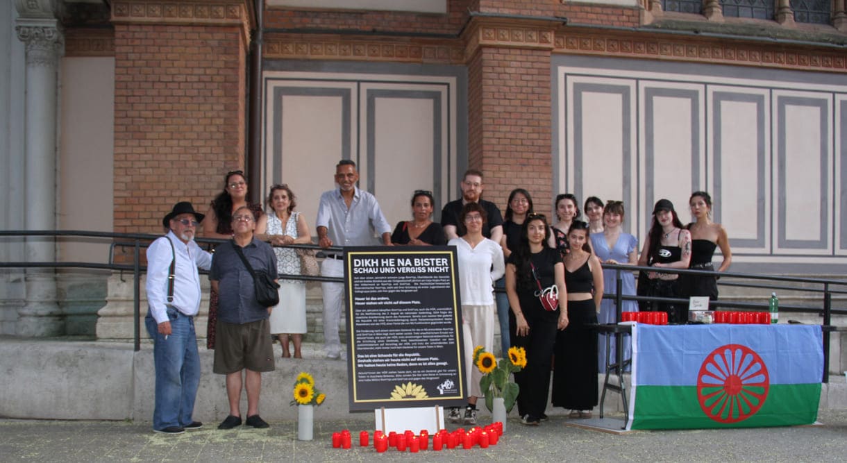 Aktivist:innen und Gedenk-Gäst:innen zwischen Kirche und Plakat sowie Infotisch