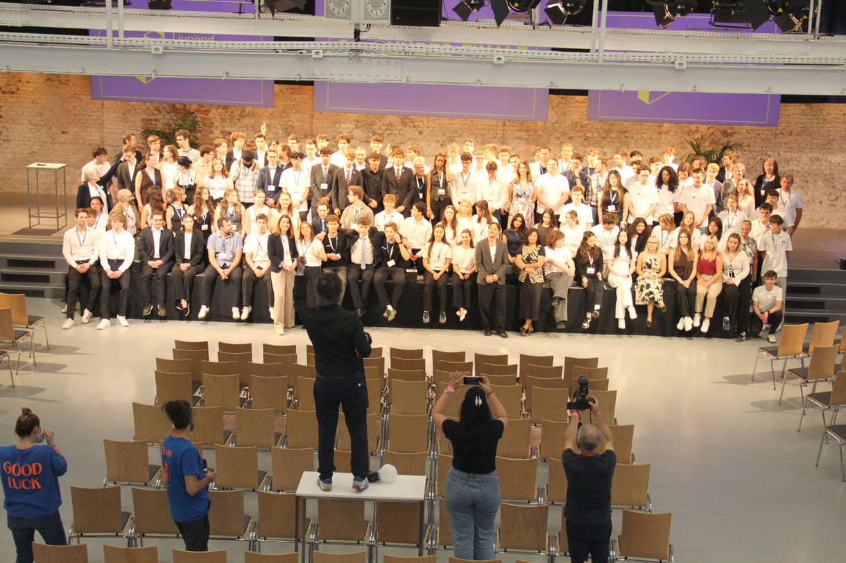 Alle - am dritten Tag in der Früh - anwesenden Teilnehmer:innen am 39. Bundesfinale von Jugend Innovativ auf einem Großgruppenfoto - von der Galerie oben - im Vordergrund: Fotograf und organisierende Personen