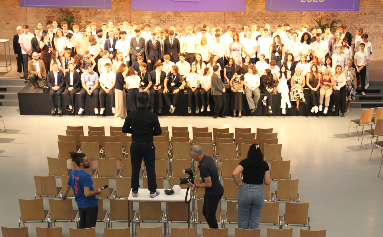 Alle - am dritten Tag in der Früh - anwesenden Teilnehmer:innen am 39. Bundesfinale von Jugend Innovativ auf einem Großgruppenfoto - von der Galerie oben - im Vordergrund: Fotograf und organisierende Personen
