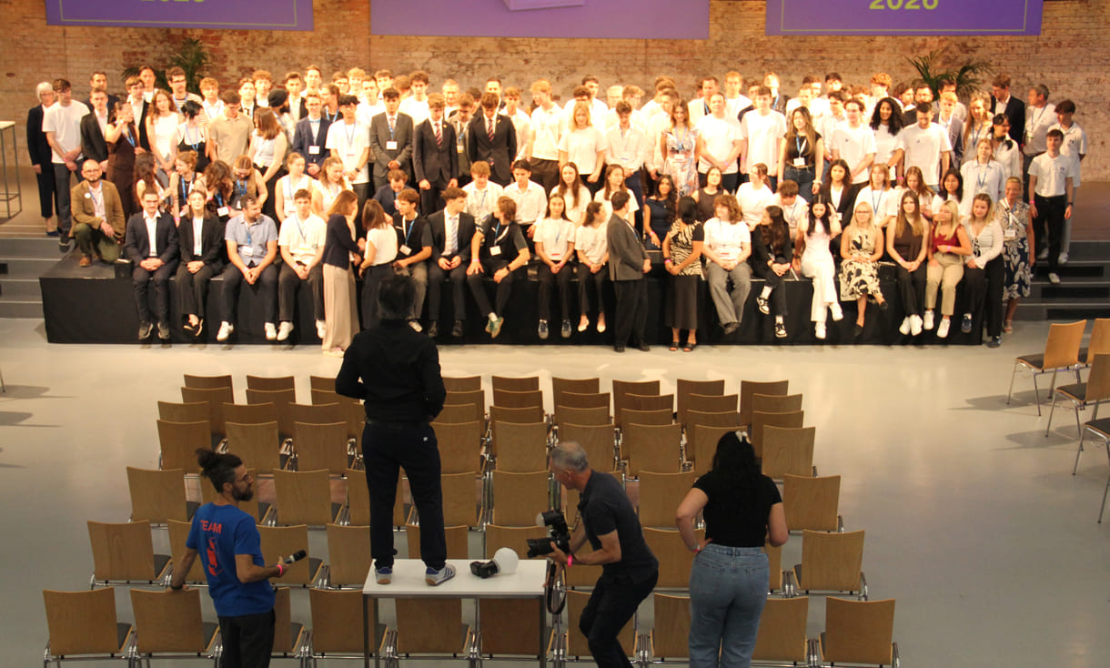 Alle - am dritten Tag in der Früh - anwesenden Teilnehmer:innen am 39. Bundesfinale von Jugend Innovativ auf einem Großgruppenfoto - von der Galerie oben - im Vordergrund: Fotograf und organisierende Personen
