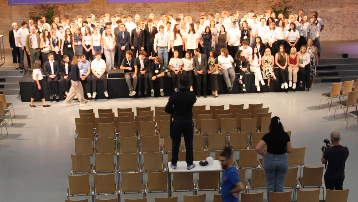 Alle - am dritten Tag in der Früh - anwesenden Teilnehmer:innen am 39. Bundesfinale von Jugend Innovativ auf einem Großgruppenfoto - von der Galerie oben - im Vordergrund: Fotograf und organisierende Personen