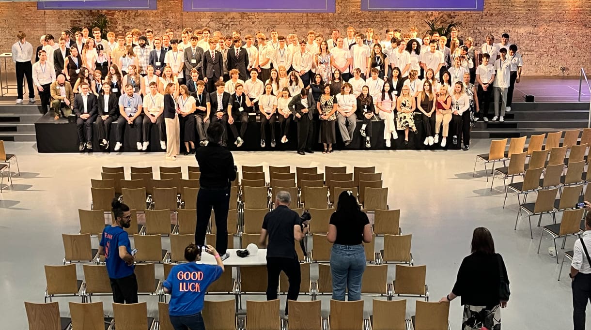 Alle - am dritten Tag in der Früh - anwesenden Teilnehmer:innen am 39. Bundesfinale von Jugend Innovativ auf einem Großgruppenfoto - von der Galerie oben - im Vordergrund: Fotograf und organisierende Personen