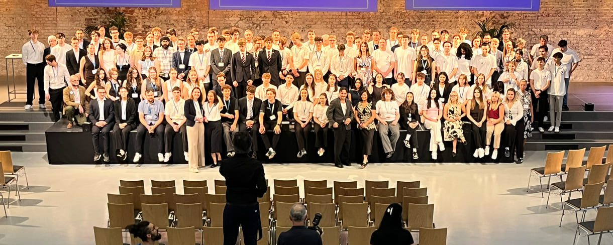 Alle - am dritten Tag in der Früh - anwesenden Teilnehmer:innen am 39. Bundesfinale von Jugend Innovativ auf einem Großgruppenfoto - von der Galerie oben - im Vordergrund: Fotograf und organisierende Personen