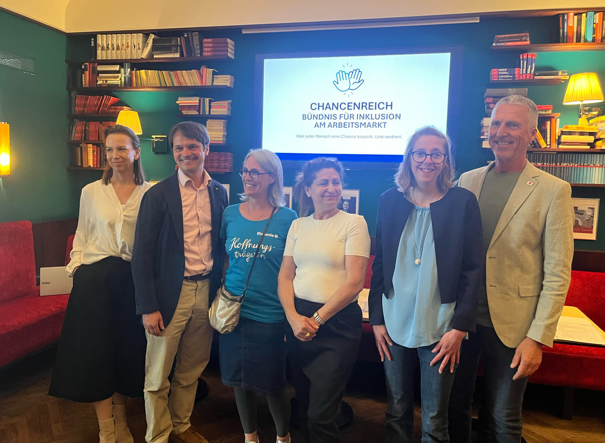 Das Podium des Mediengesprächs in einem Gruppenfoto: Von links nach rechts: Anna Parr (Generalsekretärin Caritas Österreich), Philippe Narval (Generalsekretär Lebenshilfe Österreich), Roberta Rastl (Pressesprecherin der Diakonie Österreich), Lina Kasapoğlu (Inhaberin Café Insieme in Schwaz, Tirol), Verena Köll (Arbeitnehmerin im Café Insieme), Andreas Jesse (Vorstand dabei-austria, Geschäftsführer autArK) mit dem Schriftzug und dem Logo des neuen Bündnisses 