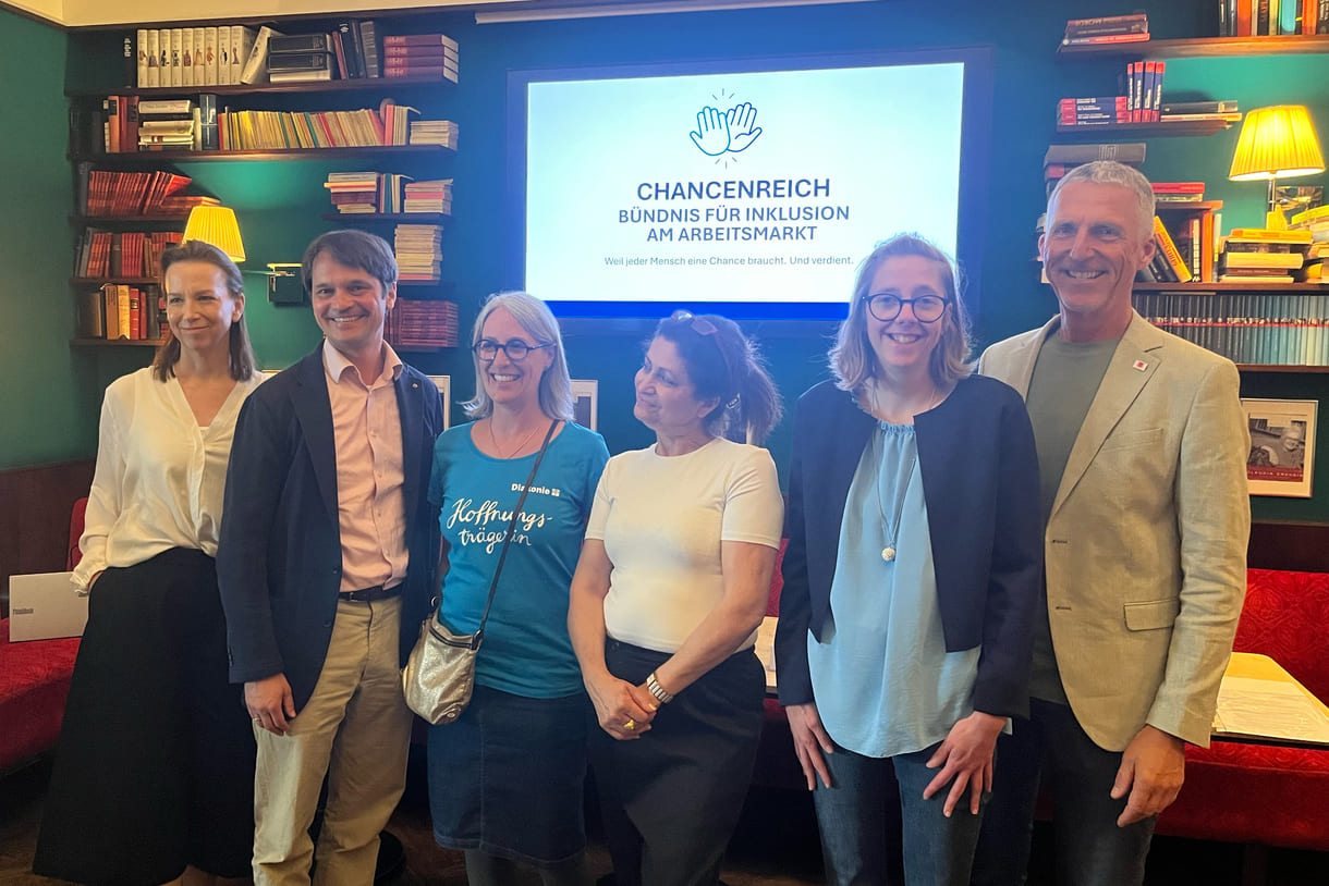Das Podium des Mediengesprächs in einem Gruppenfoto: Von links nach rechts: Anna Parr (Generalsekretärin Caritas Österreich), Philippe Narval (Generalsekretär Lebenshilfe Österreich), Roberta Rastl (Pressesprecherin der Diakonie Österreich), Lina Kasapoğlu (Inhaberin Café Insieme in Schwaz, Tirol), Verena Köll (Arbeitnehmerin im Café Insieme), Andreas Jesse (Vorstand dabei-austria, Geschäftsführer autArK) mit dem Schriftzug und dem Logo des neuen Bündnisses 