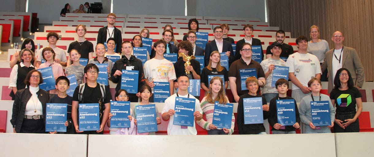 Gruppenfoto aller Preisträger:innen, die nach Linz kommen konnten, mit Jurymitgliedern und Preis-Überreicher:innen