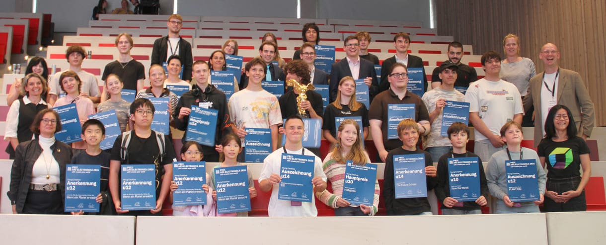Gruppenfoto aller Preisträger:innen, die nach Linz kommen konnten, mit Jurymitgliedern und Preis-Überreicher:innen